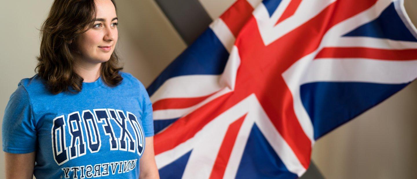 一个女孩穿着牛津大学的衬衫，在一面英国国旗前摆姿势.